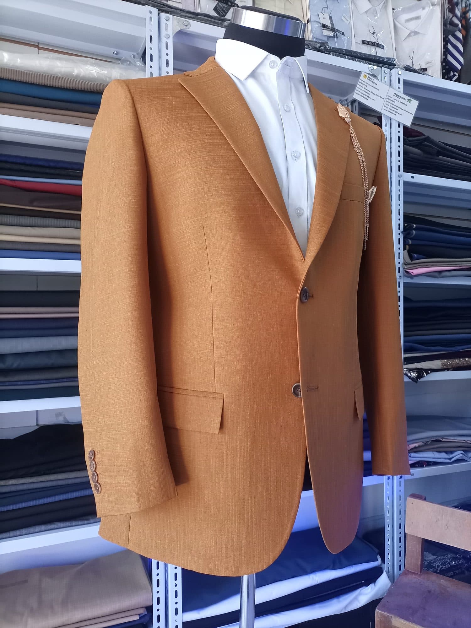 Saco color mostaza en un maniquí, frente a los estantes de telas de la sastrería